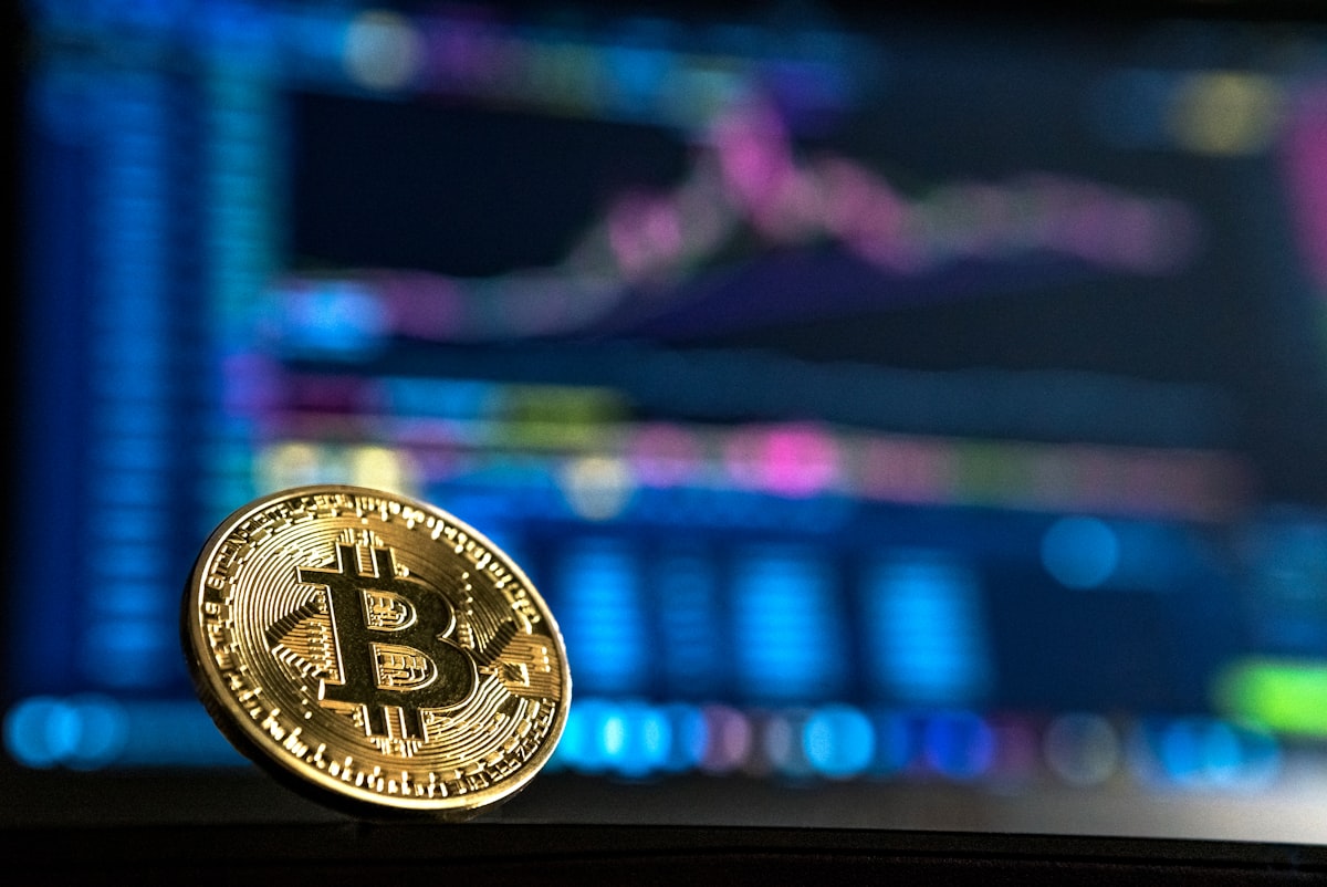 A physical bitcoin in front of a trading screen
